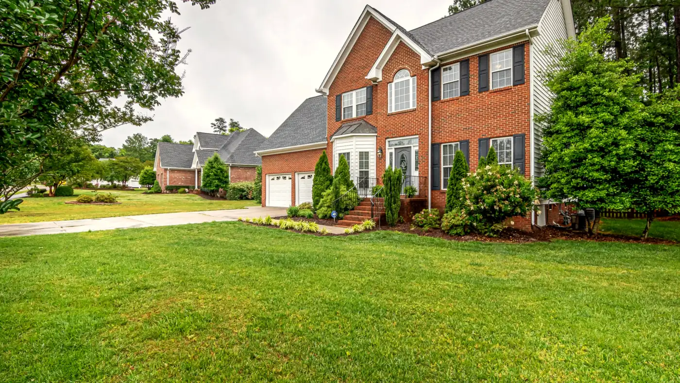 A brick two-story home with a freshly mowed lawn, trimmed foundation shrubs and mulched beds
